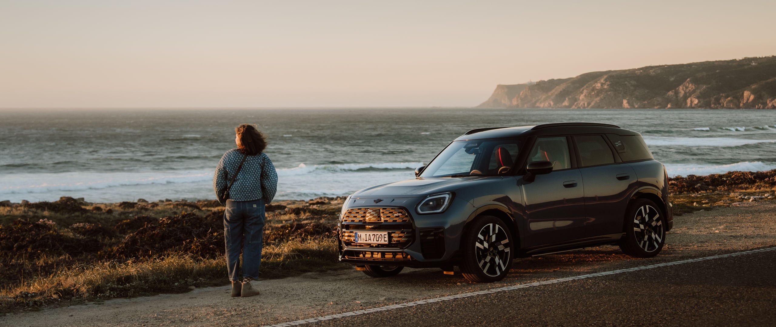 MINI Countryman am Straßenrand. Im Hintergrund das Meer & eine Landzunge.